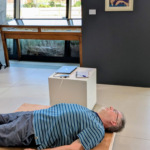 Andrew Hugill lying on a wooden vibrating floor in a gallery setting.